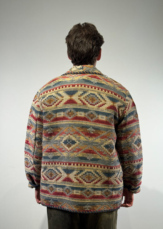 "A model wearing the Shme-Shno tapestry-inspired heritage Teprac jacket, crafted in Canada using the Hungarian Varrni technique with authentic folk patterns and rich, traditional colors. The low-button, 100% wool blazer blends Budapest’s textile heritage with contemporary Canadian tailoring, creating a bold, culturally rooted statement piece."
