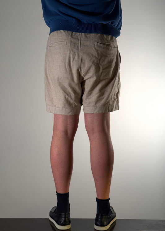 Beige linen summer shorts by Shme-Shno, a Hungarian fashion brand founded in Budapest and crafted in Canada using the traditional Varrni stitching technique. Lightweight, breathable design with a tailored fit and minimalist geometric embroidery. A refined blend of heritage craftsmanship and contemporary style.
