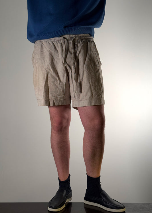 Beige linen summer shorts by Shme-Shno, a Hungarian fashion brand founded in Budapest and crafted in Canada using the traditional Varrni stitching technique. Lightweight, breathable design with a tailored fit and minimalist geometric embroidery. A refined blend of heritage craftsmanship and contemporary style.